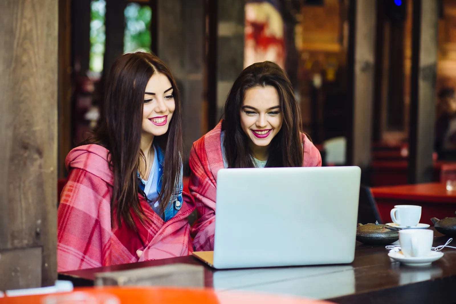 Two young beautiful girl sitting table looking something internet